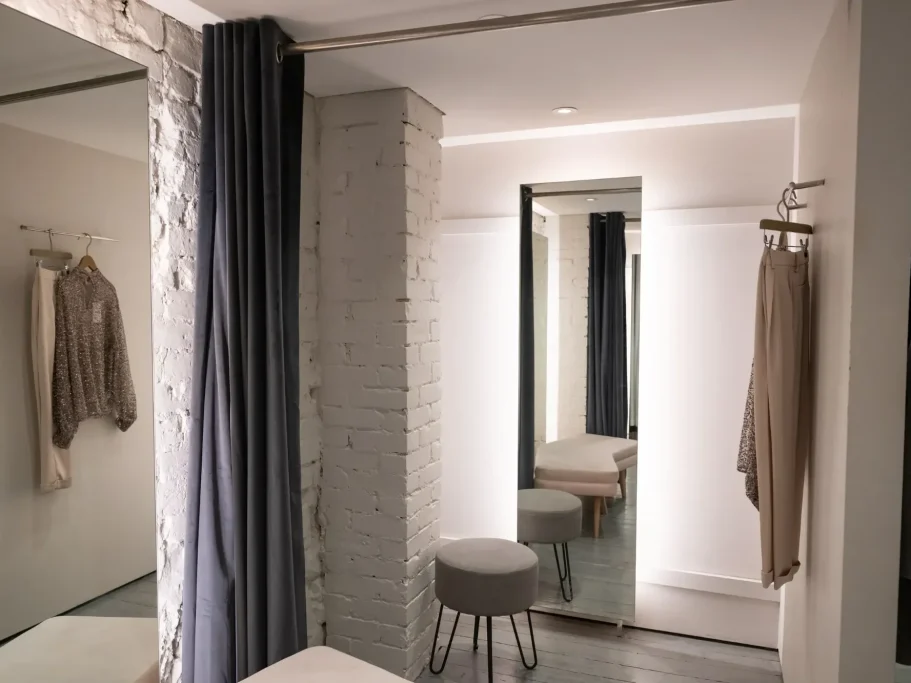 Minimalist fitting room with mirrors, soft lighting, and neutral-coloured garments